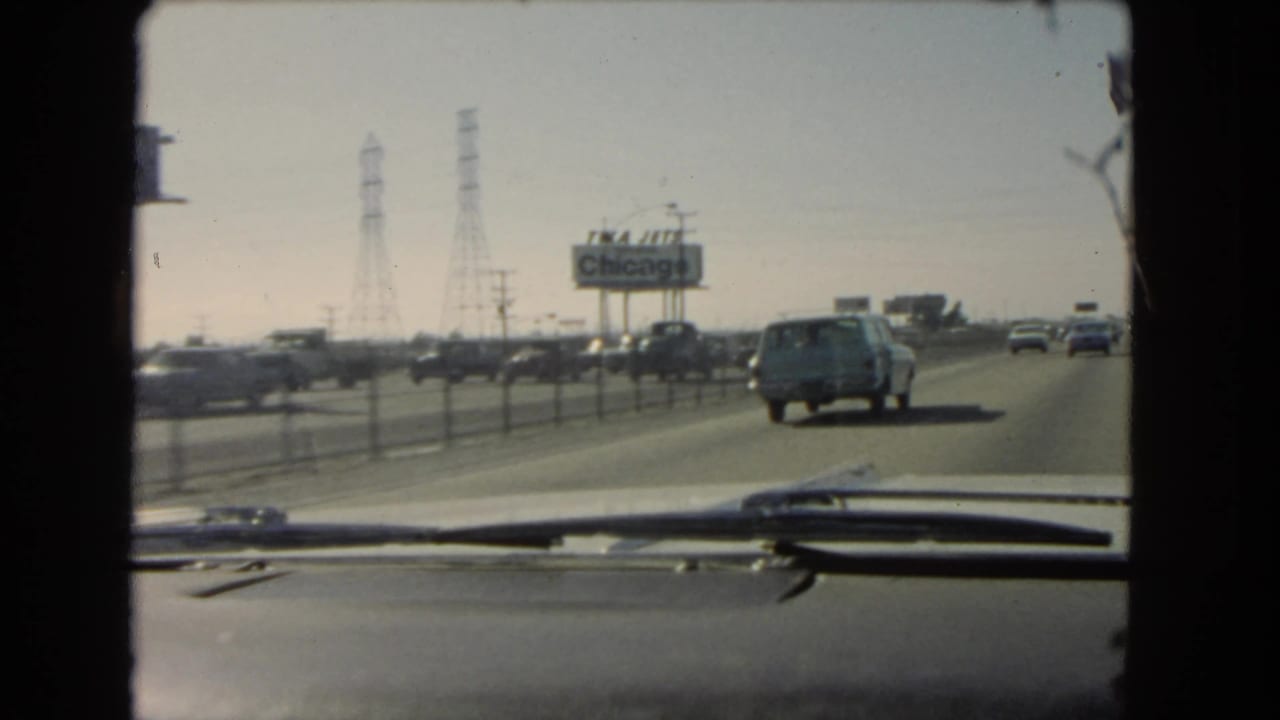 Highway view through a car windshield with traffic, a station wagon, power towers, and a Chicago billboard.