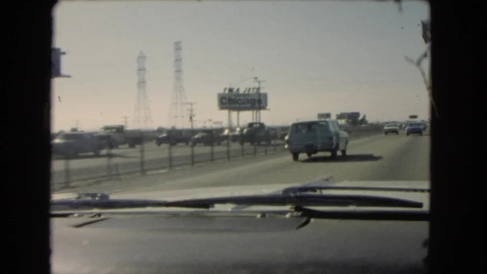 1966 California home-movie view from inside a moving car, showing highway traffic, a station wagon, power towers, and a TWA Jets Chicago billboard.