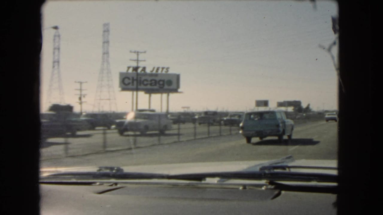 Highway traffic passes a TWA Jets Chicago billboard, seen through a car windshield.