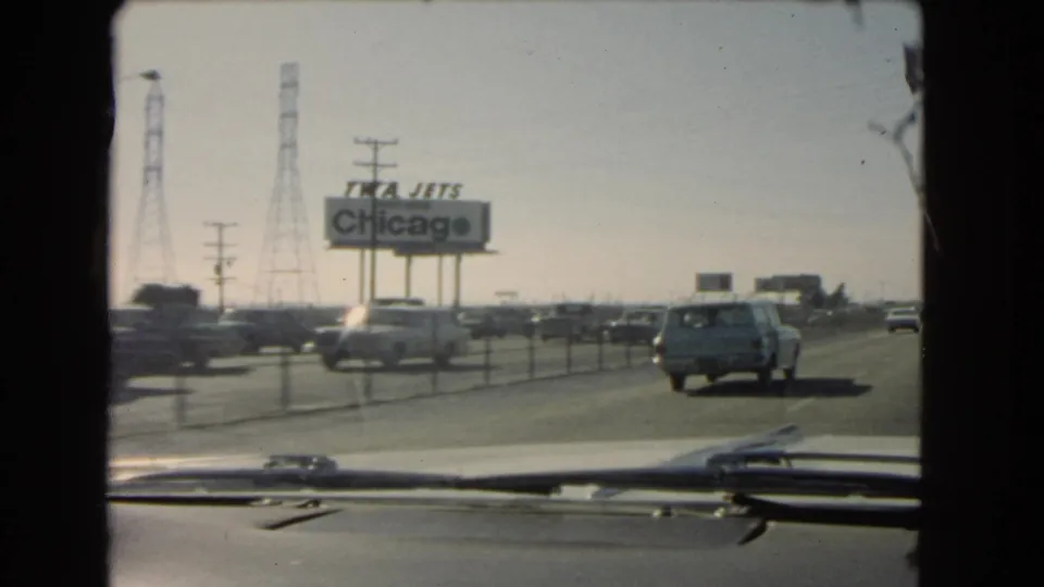 1966 California highway view from inside a moving car, with vintage traffic, dashboard trim, utility towers, and a TWA Jets Chicago billboard.