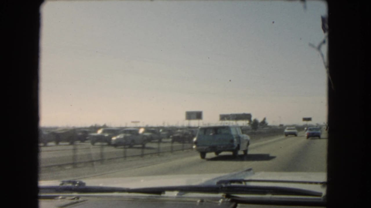Freeway traffic seen through a windshield with a station wagon ahead.