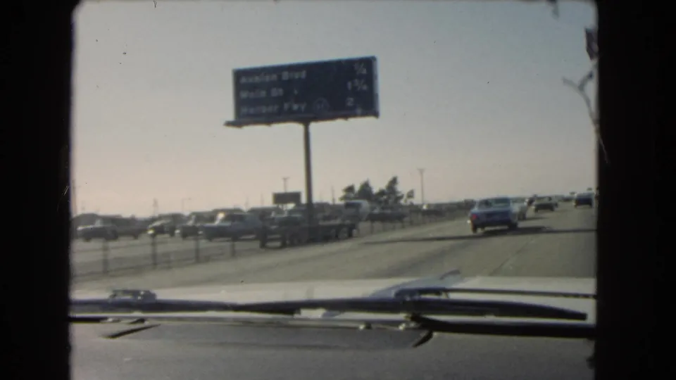 1966 California highway view showing an overhead sign for Avalon Blvd, Main St, and Harbor Fwy, with traffic seen from inside a car.