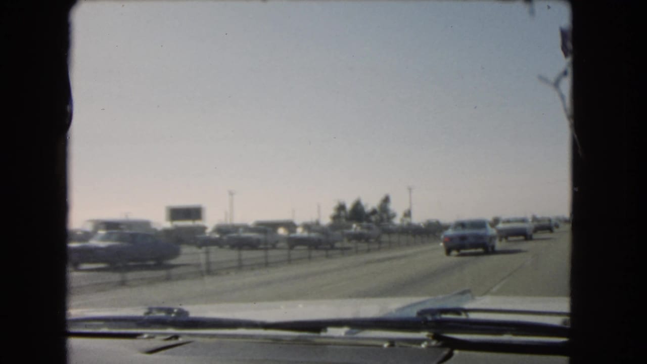 1966 California freeway traffic filmed through a car windshield, with older cars, lane dividers, and dashboard edge visible.