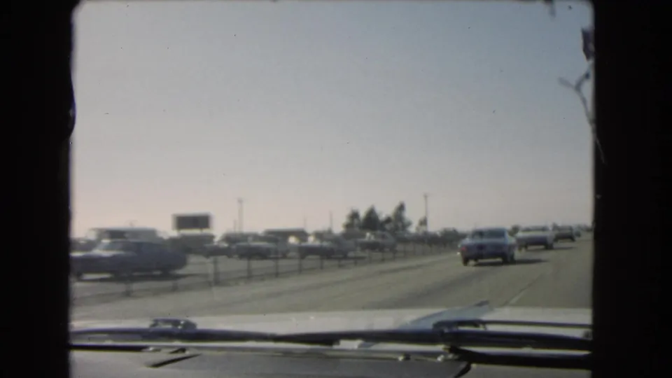 1966 California freeway traffic filmed through a car windshield, with older cars, lane dividers, and dashboard edge visible.