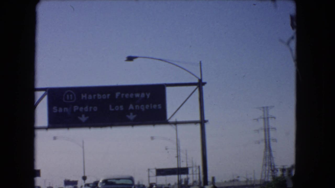 Overhead Harbor Freeway sign directing toward San Pedro and Los Angeles above a 1966 California roadway.