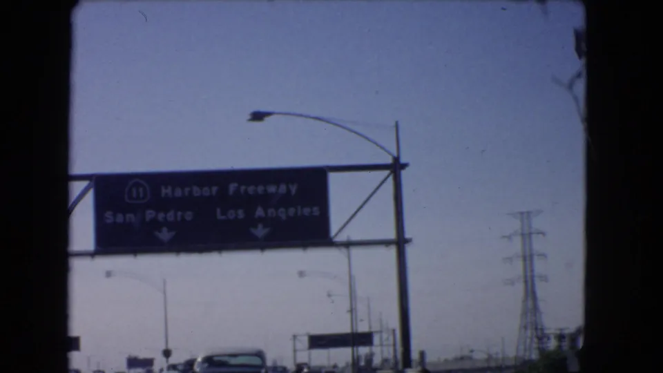 Overhead Harbor Freeway sign directing toward San Pedro and Los Angeles above a 1966 California roadway.