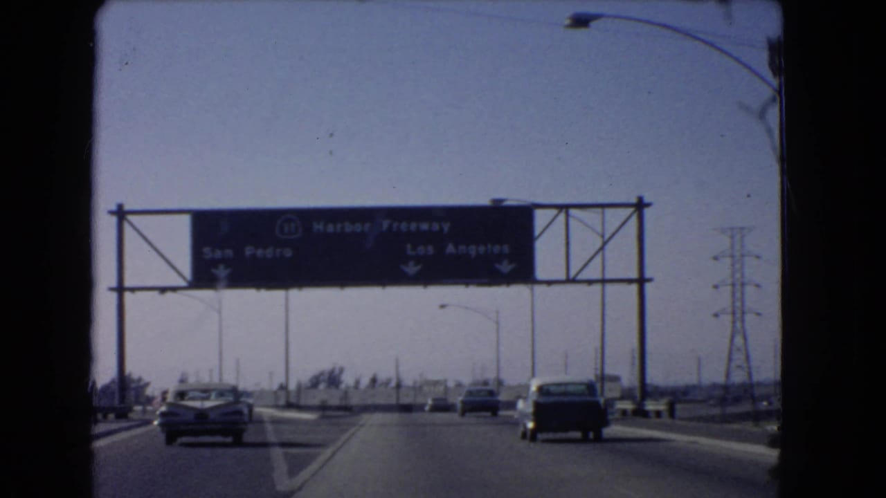 1966 windshield view of cars approaching a Harbor Freeway sign with San Pedro and Los Angeles directions.