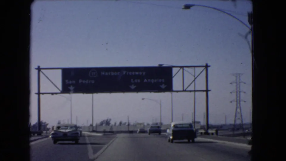 1966 windshield view of cars approaching a Harbor Freeway sign with San Pedro and Los Angeles directions.