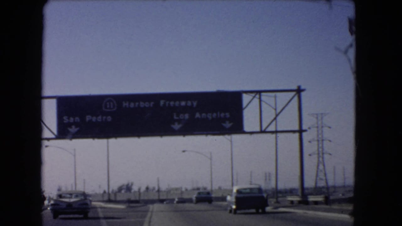 Vintage 8mm view of a California freeway sign for San Pedro and Los Angeles with cars moving below.