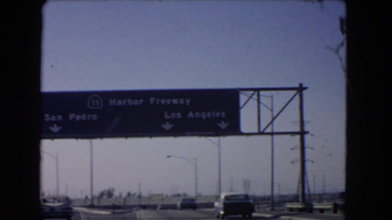 Overhead Harbor Freeway sign above moving traffic with San Pedro and Los Angeles directions.