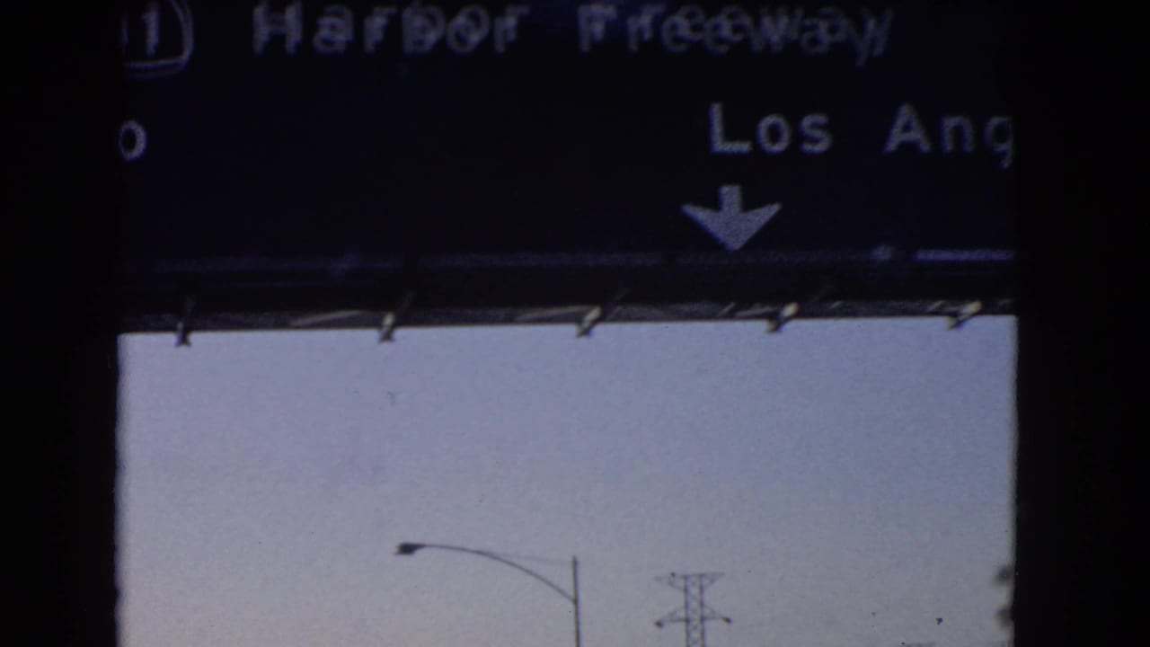 1966 California home-movie frame showing a cropped Harbor Freeway sign and roadway lights from inside a moving vehicle.