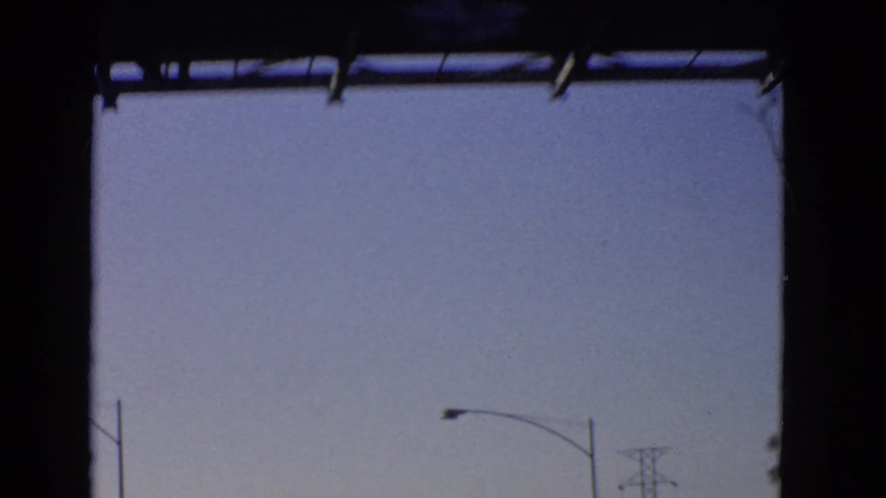 A sparse California highway view from a moving car shows blue sky, partial roadside poles, and the dark border of scanned 8mm film.