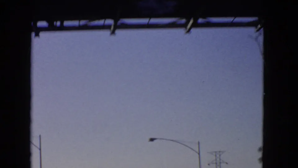 A sparse California highway view from a moving car shows blue sky, partial roadside poles, and the dark border of scanned 8mm film.