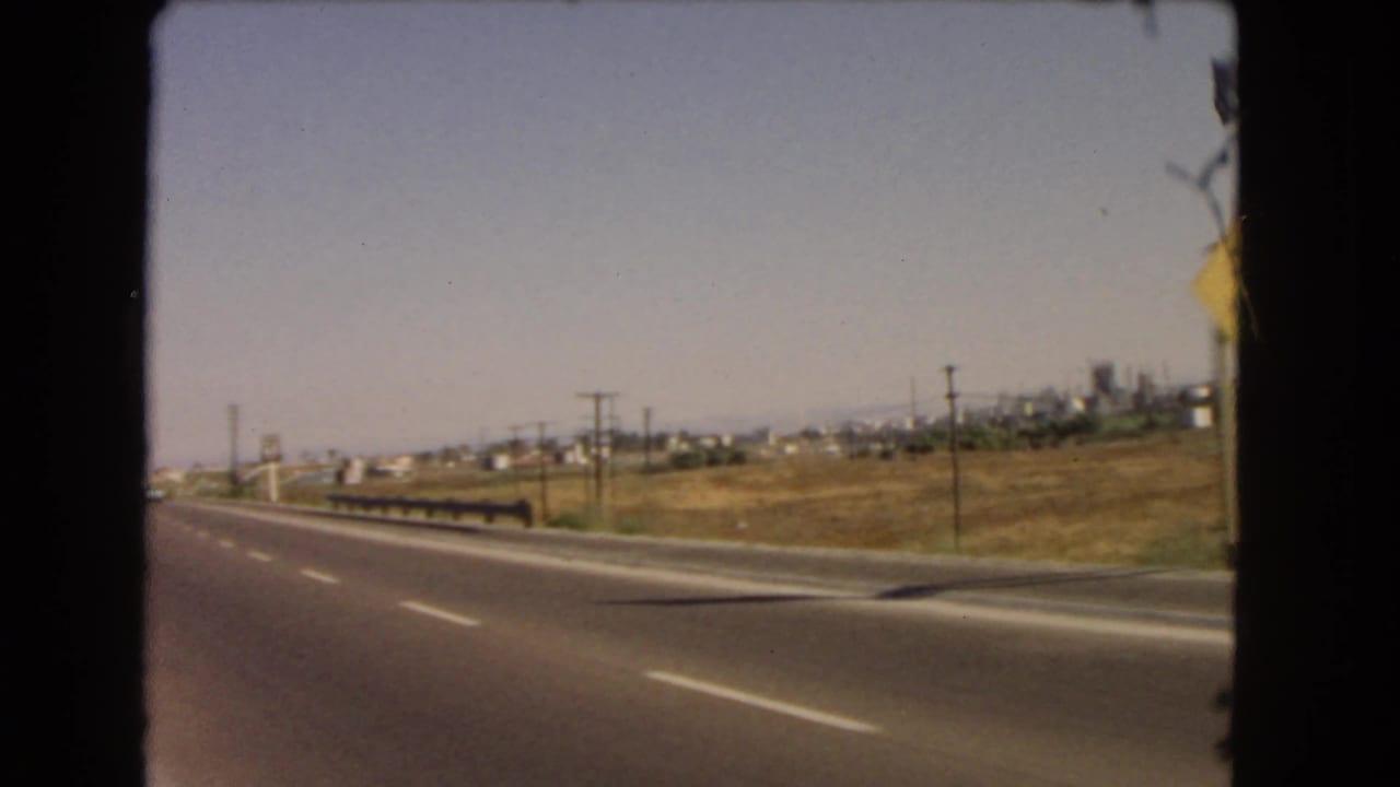 Highway lane with roadside utility poles and distant industrial-looking structures.