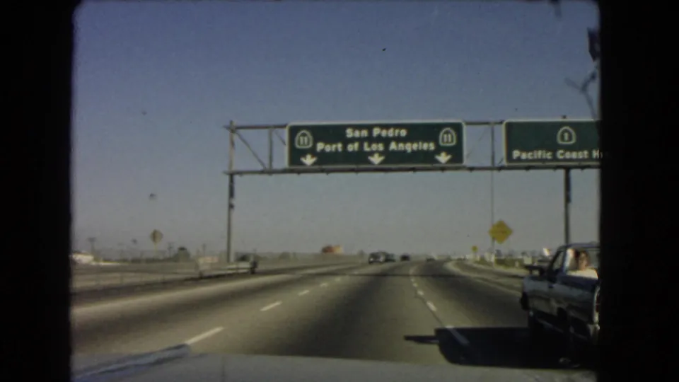 1966 California road footage shows overhead green signs for San Pedro and the Port of Los Angeles on Route 11 above a multi-lane highway.