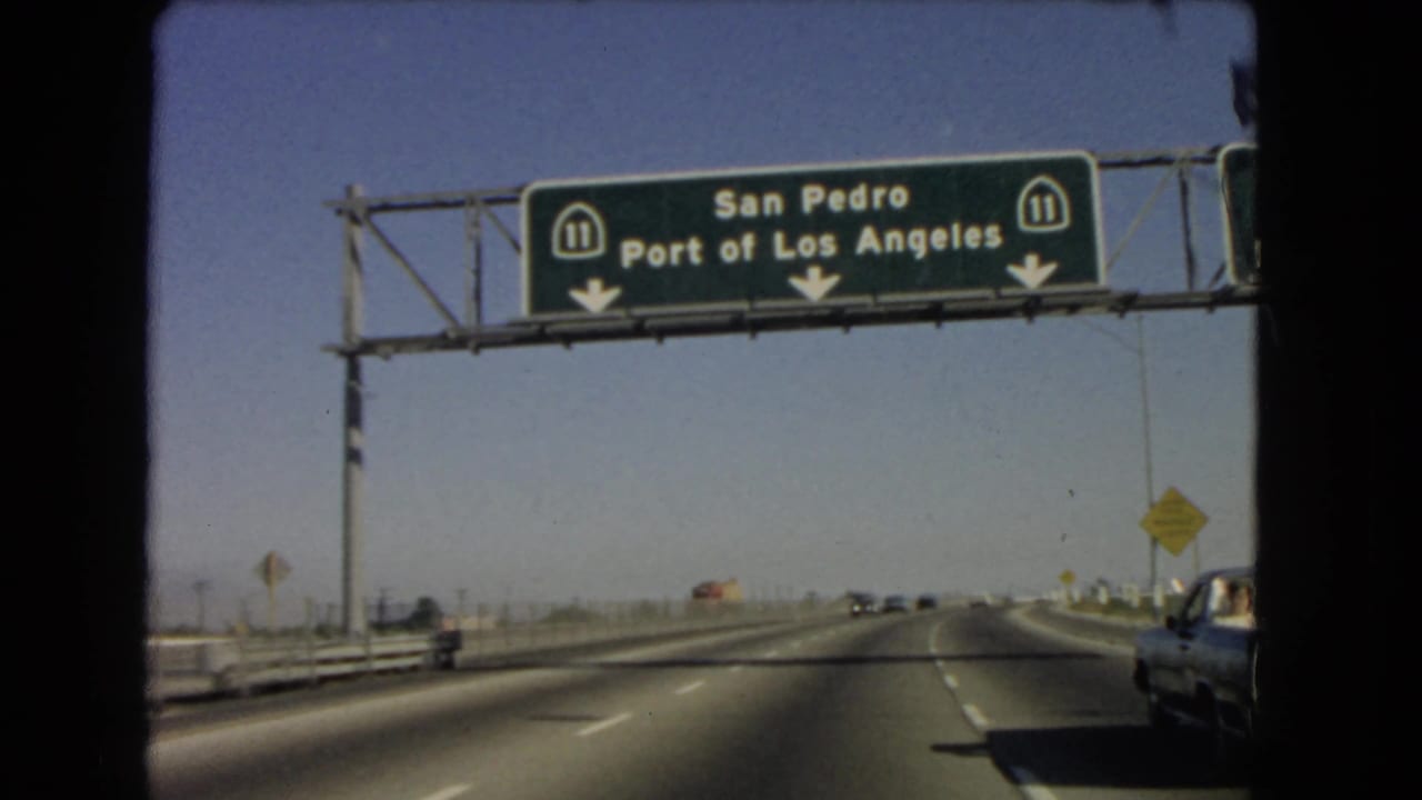 A closer passenger-seat view shows Route 11 overhead signs for San Pedro and the Port of Los Angeles, with a car partly visible in the right lane.
