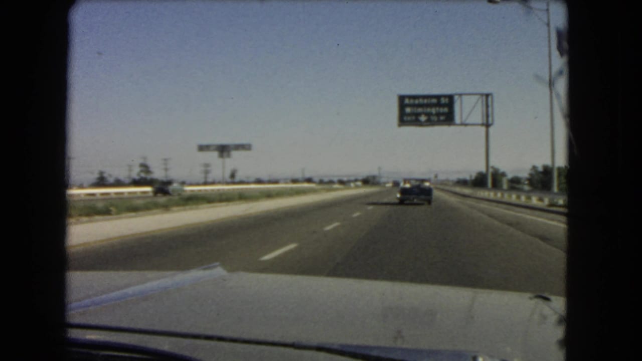 1966 California 8mm view from inside a moving car, looking down a highway toward an Anaheim St and Wilmington exit sign.