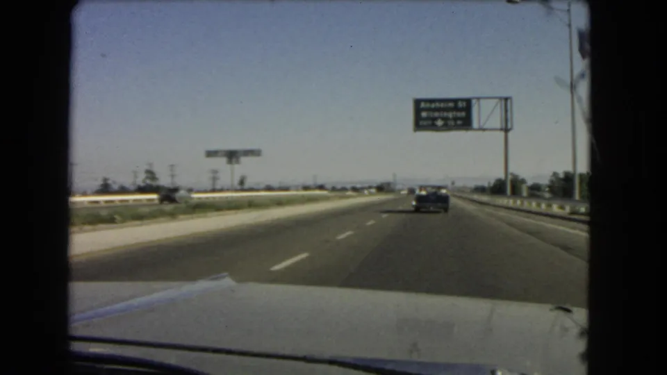 1966 California 8mm view from inside a moving car, looking down a highway toward an Anaheim St and Wilmington exit sign.