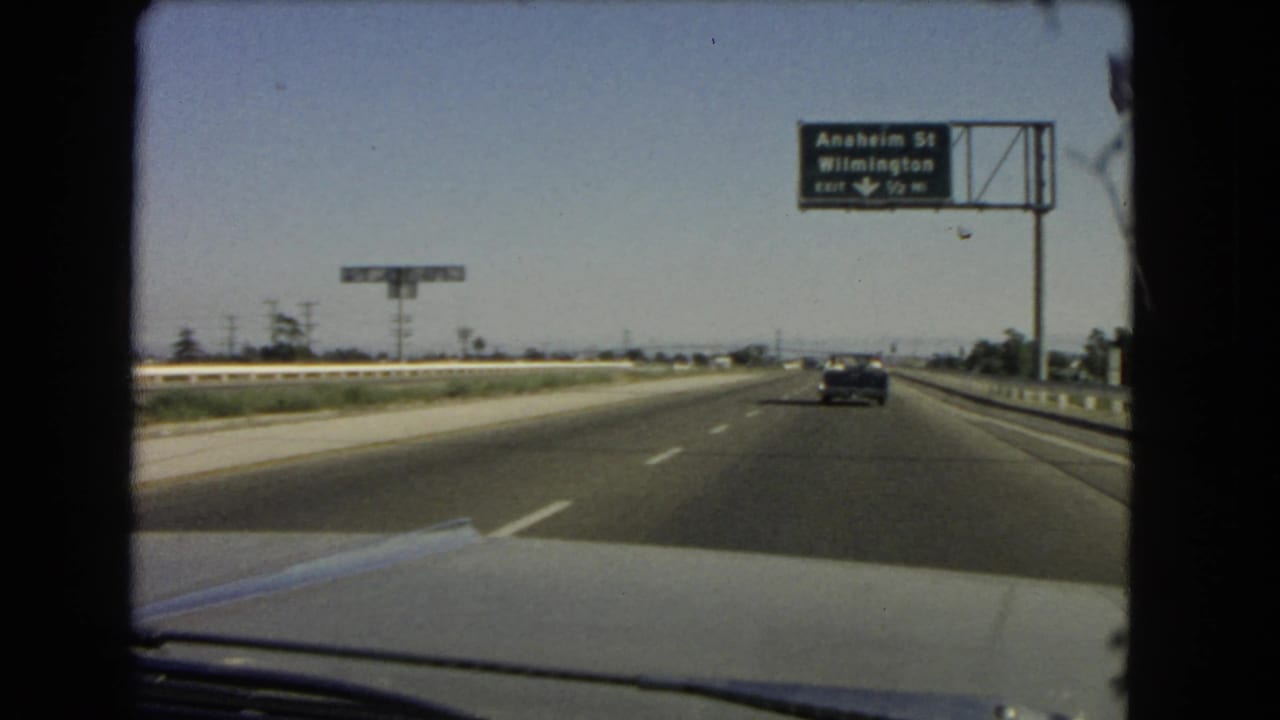 Moving-car view on a California highway, with light traffic and a green sign for Anaheim St and Wilmington visible ahead.