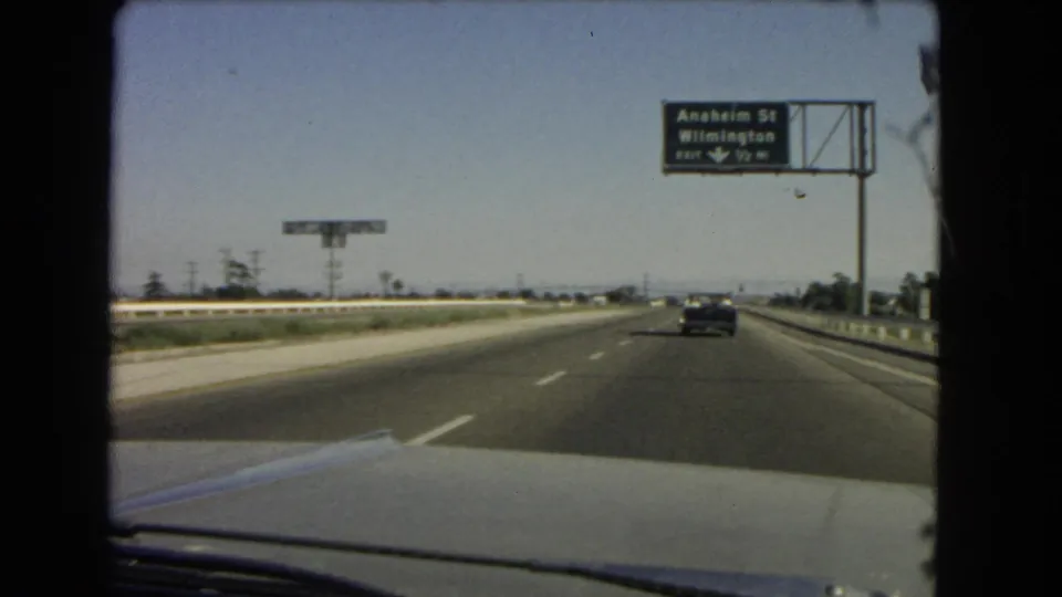 Moving-car view on a California highway, with light traffic and a green sign for Anaheim St and Wilmington visible ahead.