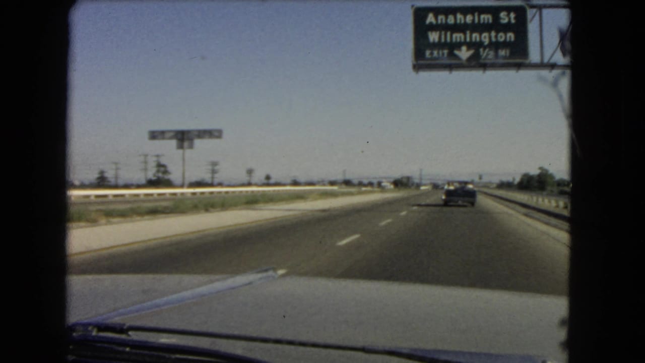 1960s windshield-view footage as the car nears or passes under an Anaheim St and Wilmington highway exit sign.
