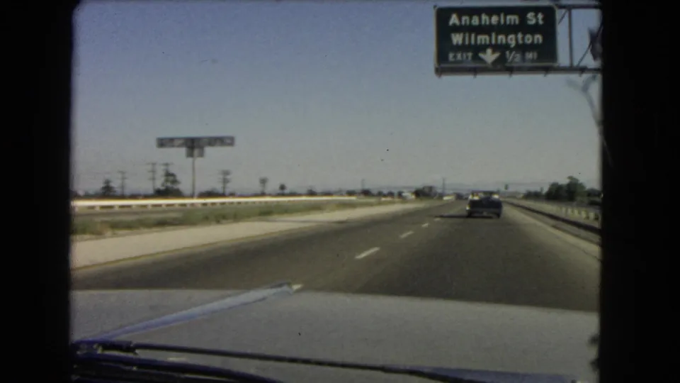 1960s windshield-view footage as the car nears or passes under an Anaheim St and Wilmington highway exit sign.