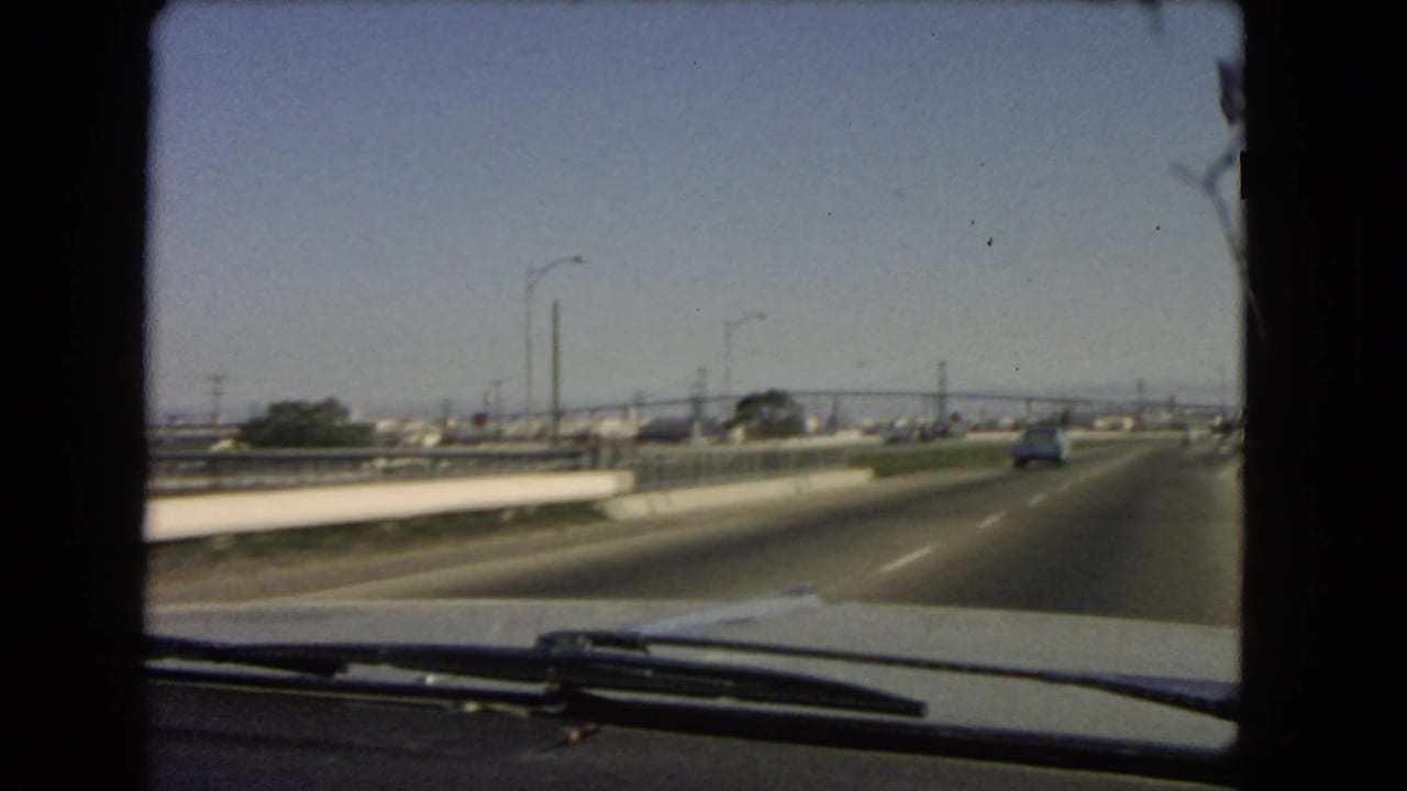 View through a car windshield on a multi-lane highway with light traffic and distant bridge structures.