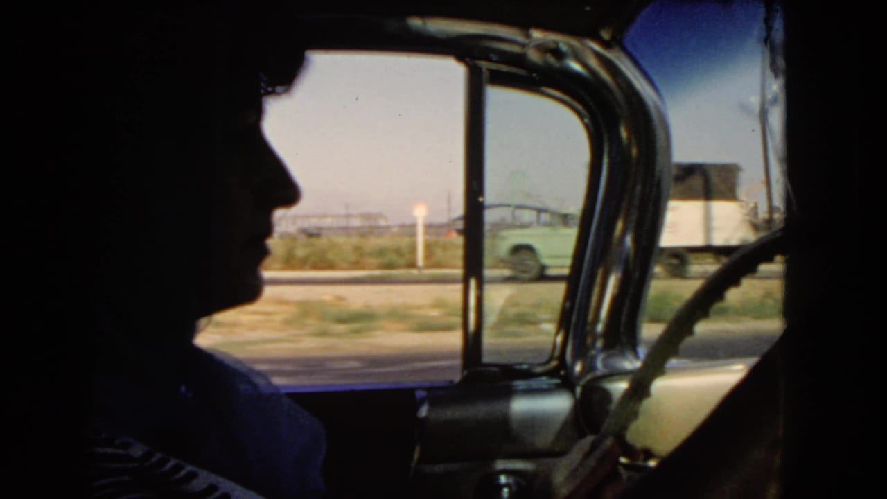 Interior 1966 California car view with a silhouetted occupant or driver, window frame, roadside, and passing vehicles outside.