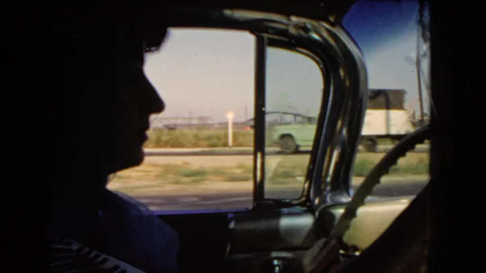 Interior 1966 California car view with a silhouetted occupant or driver, window frame, roadside, and passing vehicles outside.