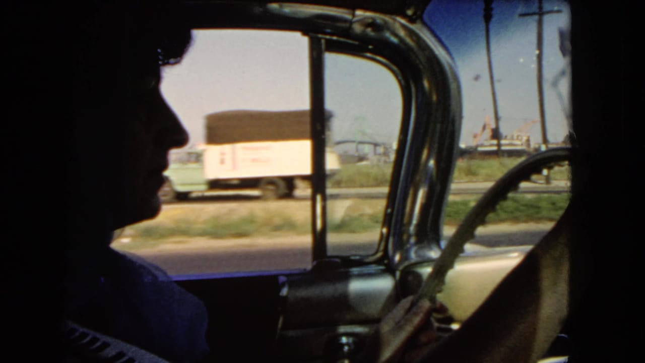Driver in silhouette inside a car with roadside truck visible through the window.