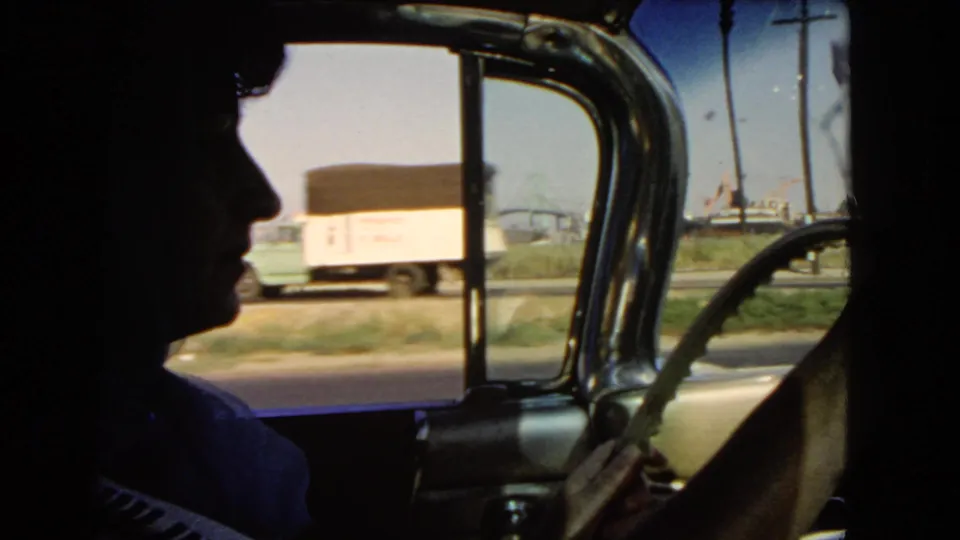 1966 California 8mm frame showing a silhouetted driver, car window, steering wheel edge, and a passing roadside truck.