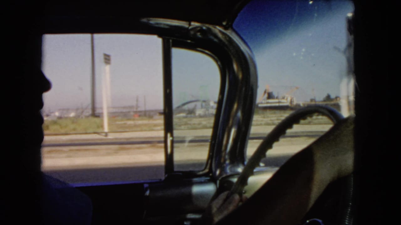 A 1966 California car interior shot shows the silhouetted driver, steering wheel, open side view, and distant roadside structures.