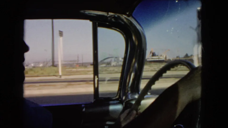 A 1966 California car interior shot shows the silhouetted driver, steering wheel, open side view, and distant roadside structures.