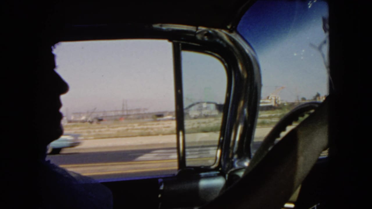 Passenger-side 8mm view from a moving car, with a person's profile silhouette and highway traffic outside in California.