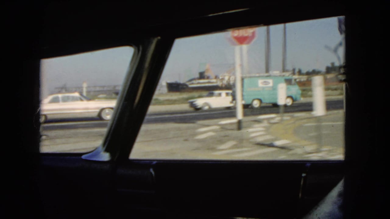 White sedan, blue delivery van, and stop sign outside a car window.
