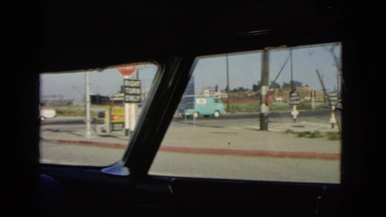 View from inside a car toward a roadside intersection with signs and a turquoise van.