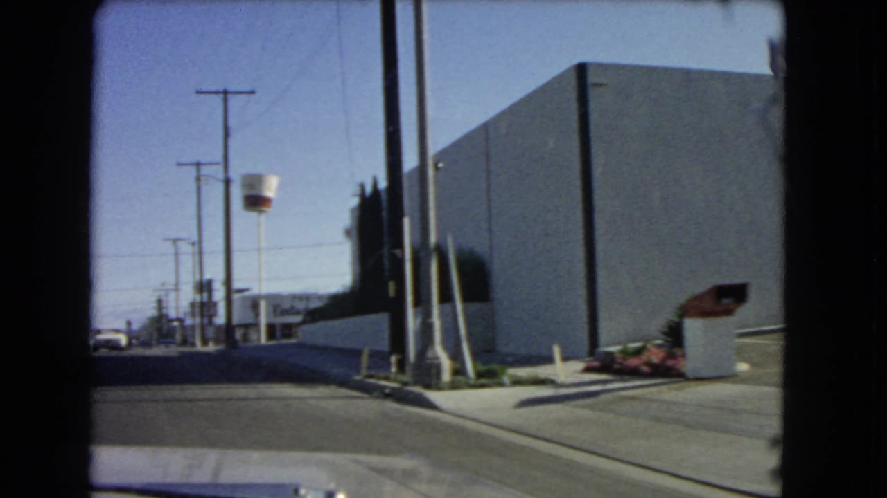 1966 California roadside frame showing a plain commercial building, utility poles, landscaping, and part of the McDonald's golden arch structure.