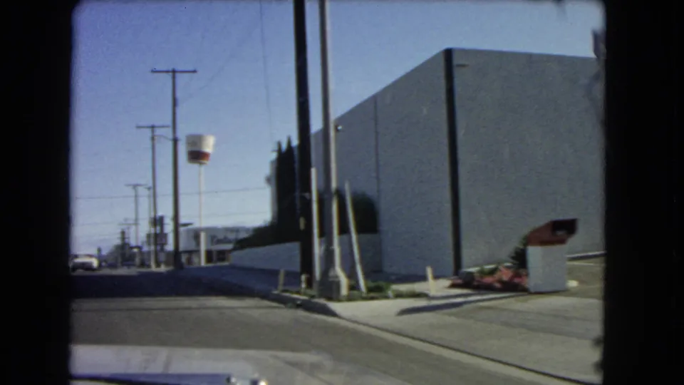 1966 California roadside frame showing a plain commercial building, utility poles, landscaping, and part of the McDonald's golden arch structure.