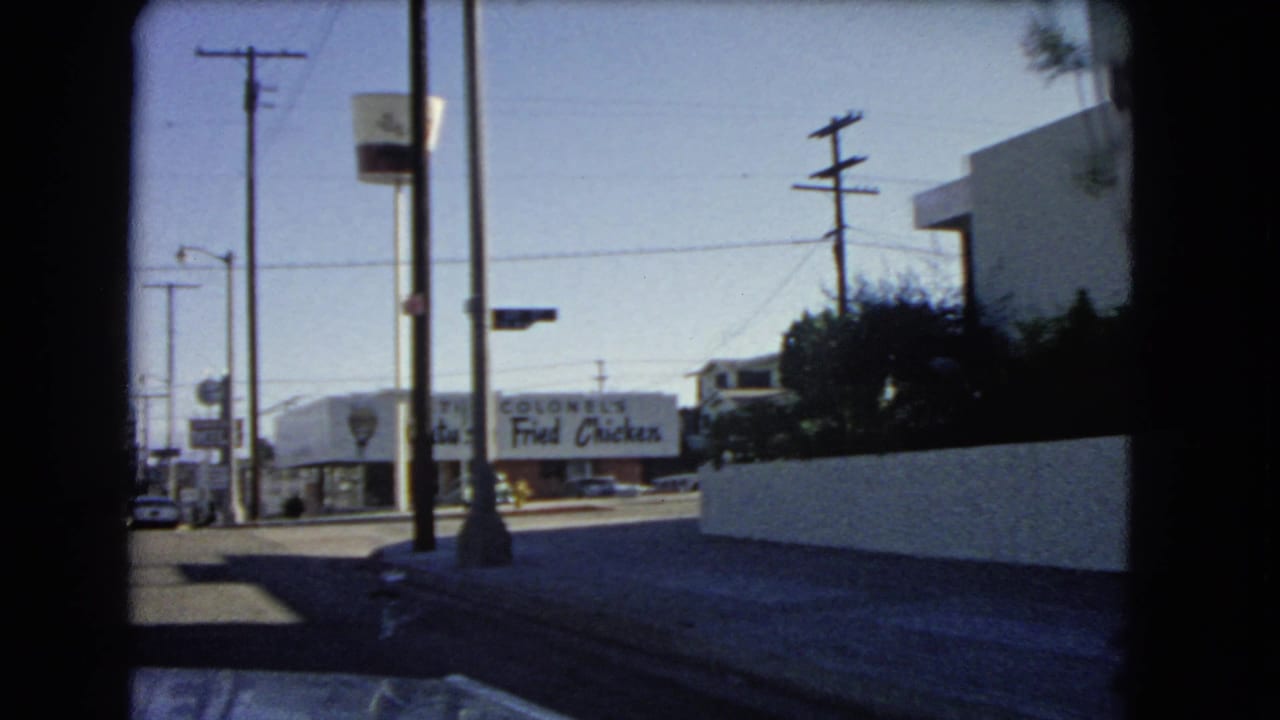 1966 California drive-by view with a visible Kentucky Fried Chicken sign, utility poles, sidewalk, and mid-century commercial buildings.