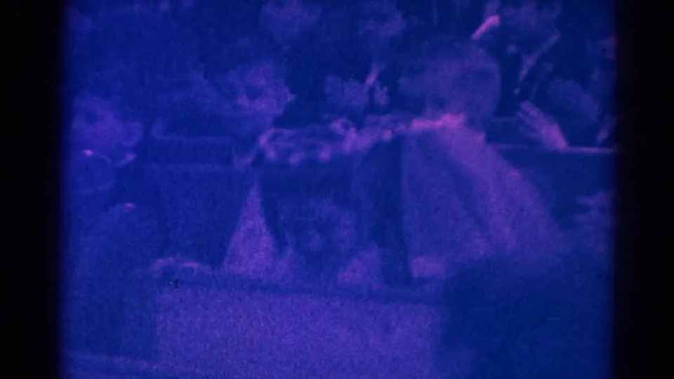 1966 Danville, Illinois church ceremony frame showing pews, a light-dressed participant, and nearby congregants in soft 8mm focus.