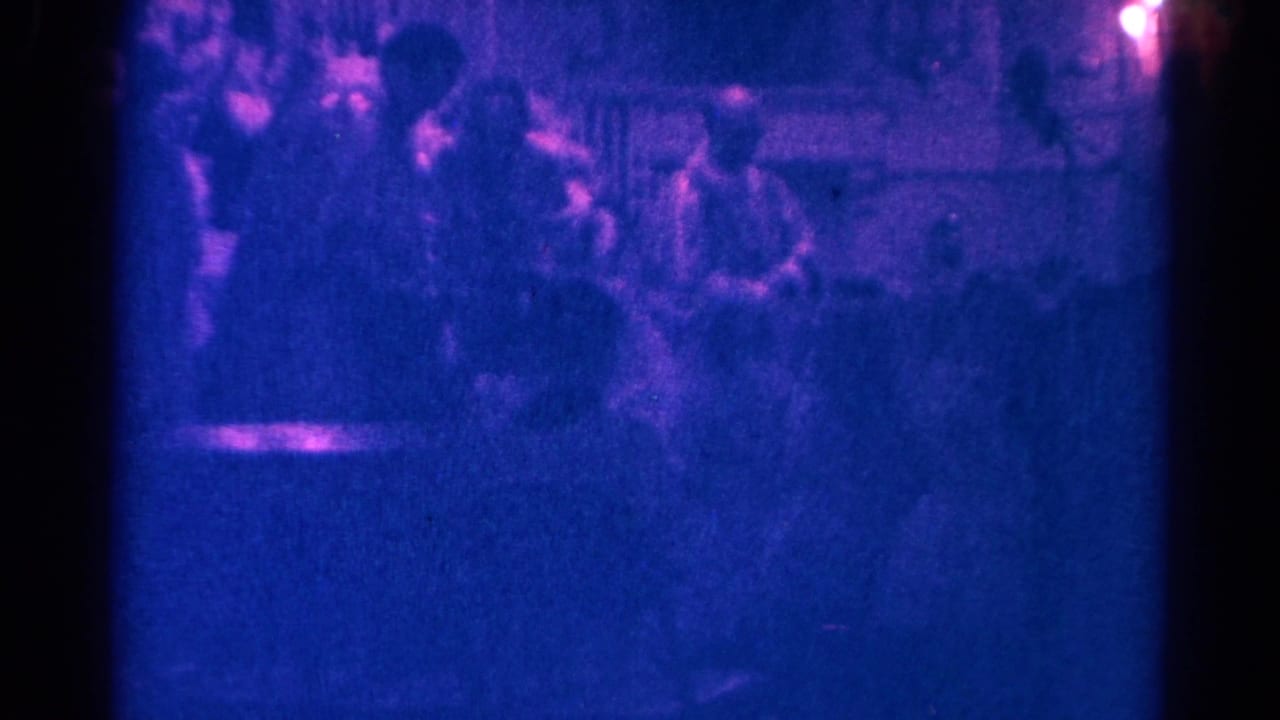 1966 Danville, Illinois 8mm frame showing indistinct seated people in a low-light indoor gathering.
