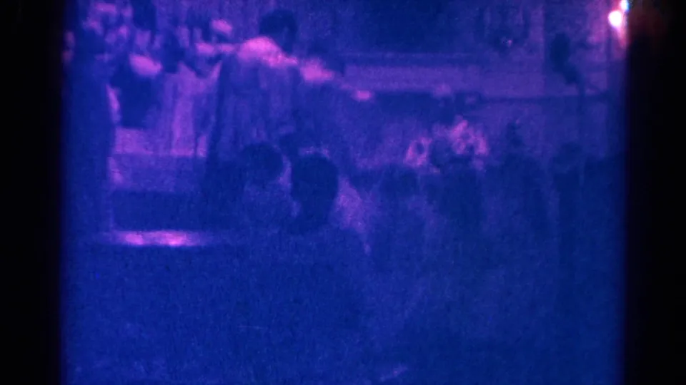 Soft 8mm frame from Danville, Illinois, showing blurred seated figures in a dark blue-purple interior space.