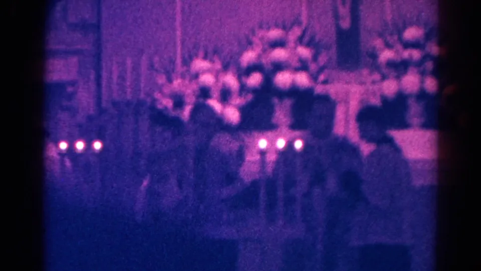 A child and attendees appear near a flowered church altar with candles in this 1966 Danville Communion footage.