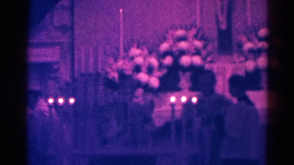 Danville, Illinois 1966 8mm frame showing candles and flowers beneath a hanging Jesus display, with worshippers in silhouette.