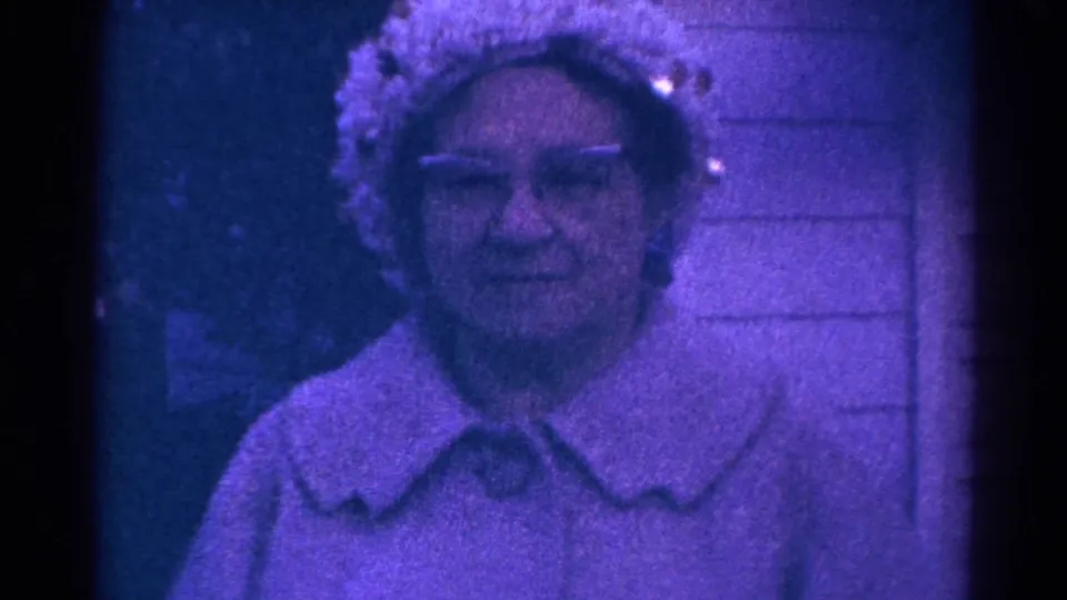 Blue-tinted 1966 home-movie portrait of an adult woman in glasses, seen near exterior siding in Danville, Illinois.