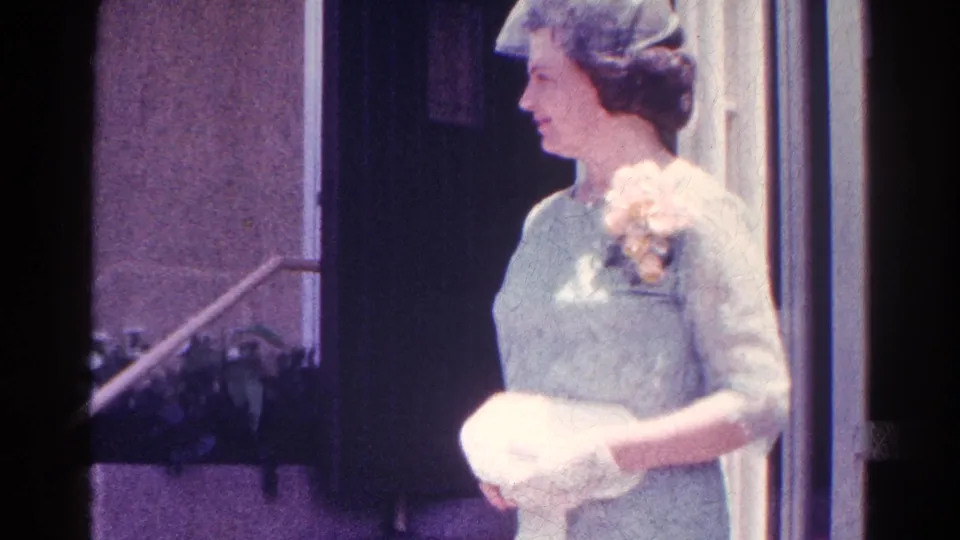 In Danville, Illinois 1966 home-movie footage, a formally dressed woman with corsage turns beside a building entrance.