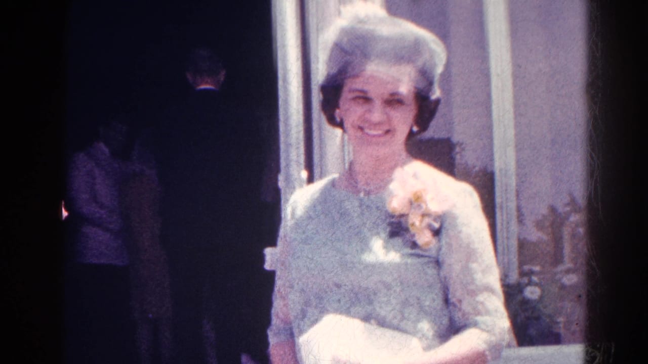A woman in a light blue lace dress and matching hat smiles toward the camera in 1966 Danville home-movie footage.