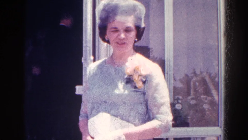 The woman remains near the entrance, with glass panels and a shadowed guest visible behind her in the 1966 Danville scene.
