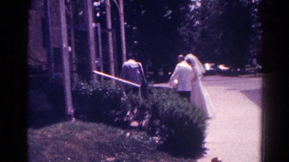 In Danville, Illinois in 1966, a bride in a veil and a groom in a light suit approach a chapel entrance beside shrubbery.
