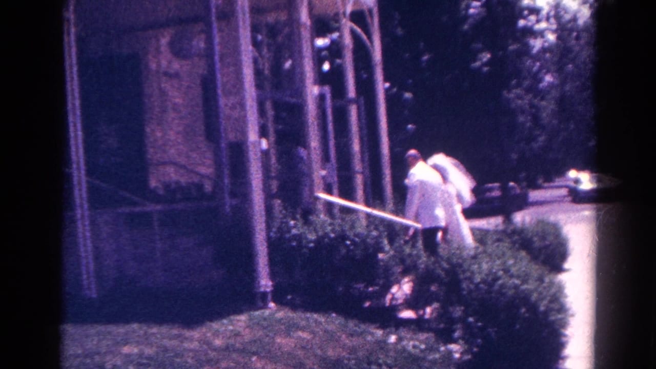 The couple continues toward the chapel entrance in the 1966 Danville wedding footage, partially framed by porch posts and bushes.